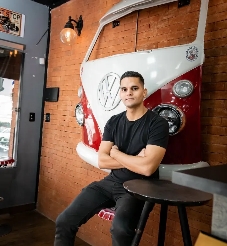 A frente de uma Kombi vermelha e branca na parede de tijolinho da barbearia